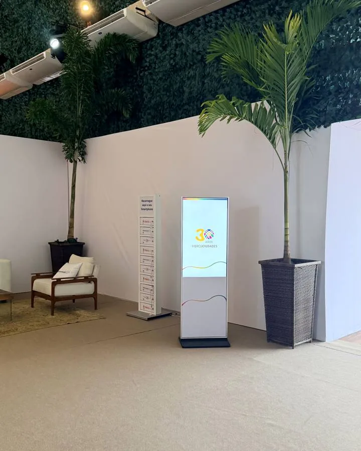 Totem interativo em lounge com parede verde e plantas em evento corporativo