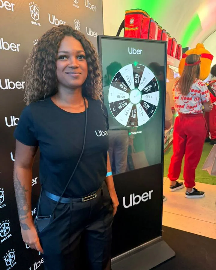 Promotora ao lado de totem interativo Uber com roleta de prêmios em ativação de evento